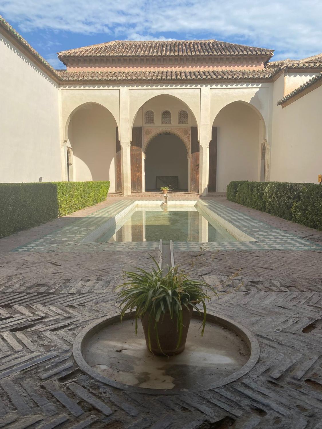 A Moorish courtyard with three arches, a long pond and two potted plants